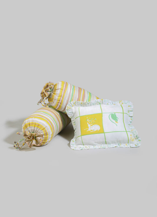 Two striped fabric bolster cushions with pastel yellow, green, and beige tones, featuring drawstring ends and ruffled edges. Additionally, a square fabric cushion with a printed design of animals and plants, edged with a ruffled border, in white, yellow, and green colors.