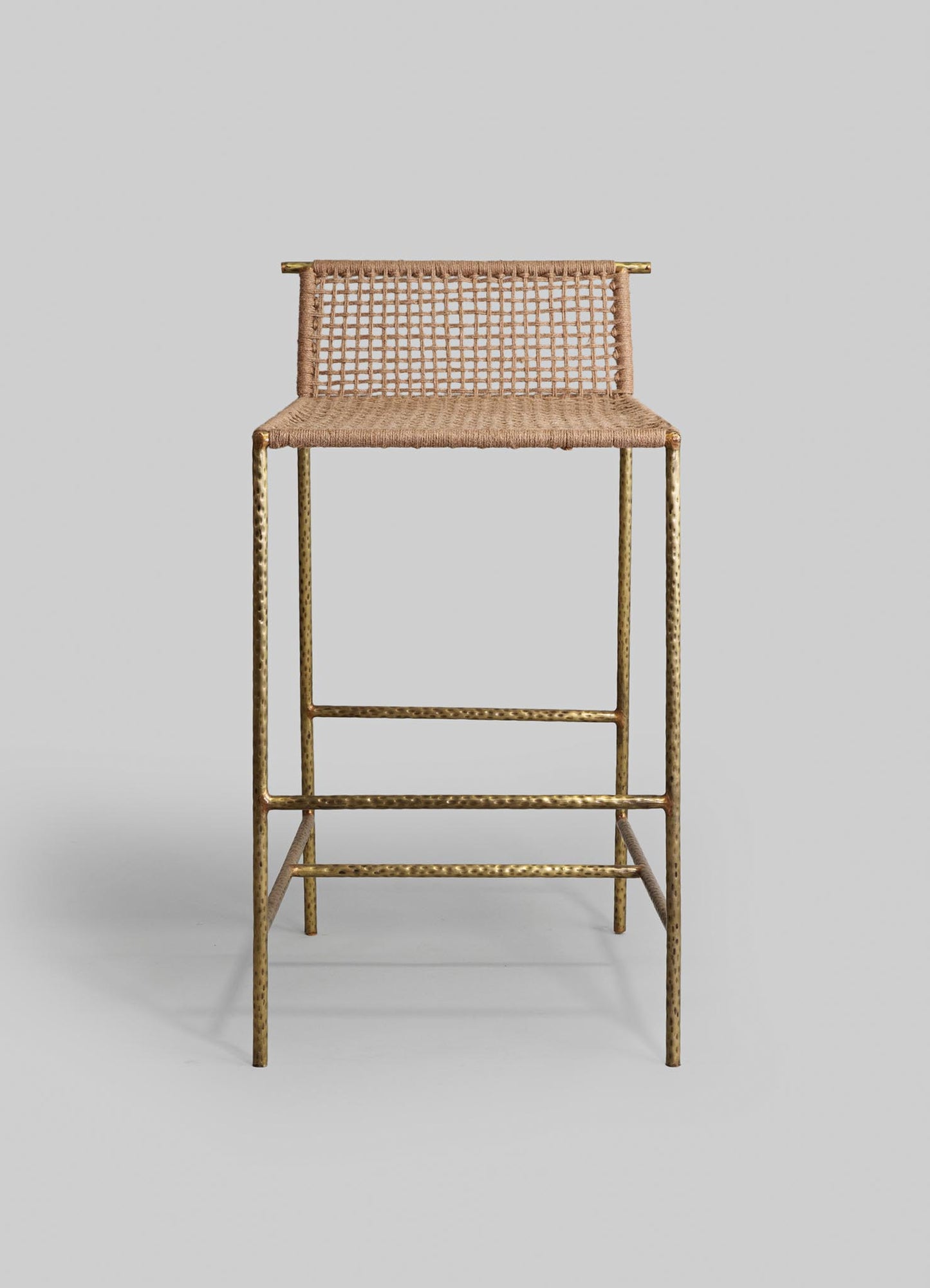 A bar stool featuring a woven rattan seat and backrest with a natural finish, supported by a gold-toned hammered metal frame. The design combines rustic craftsmanship with contemporary metallic accents.