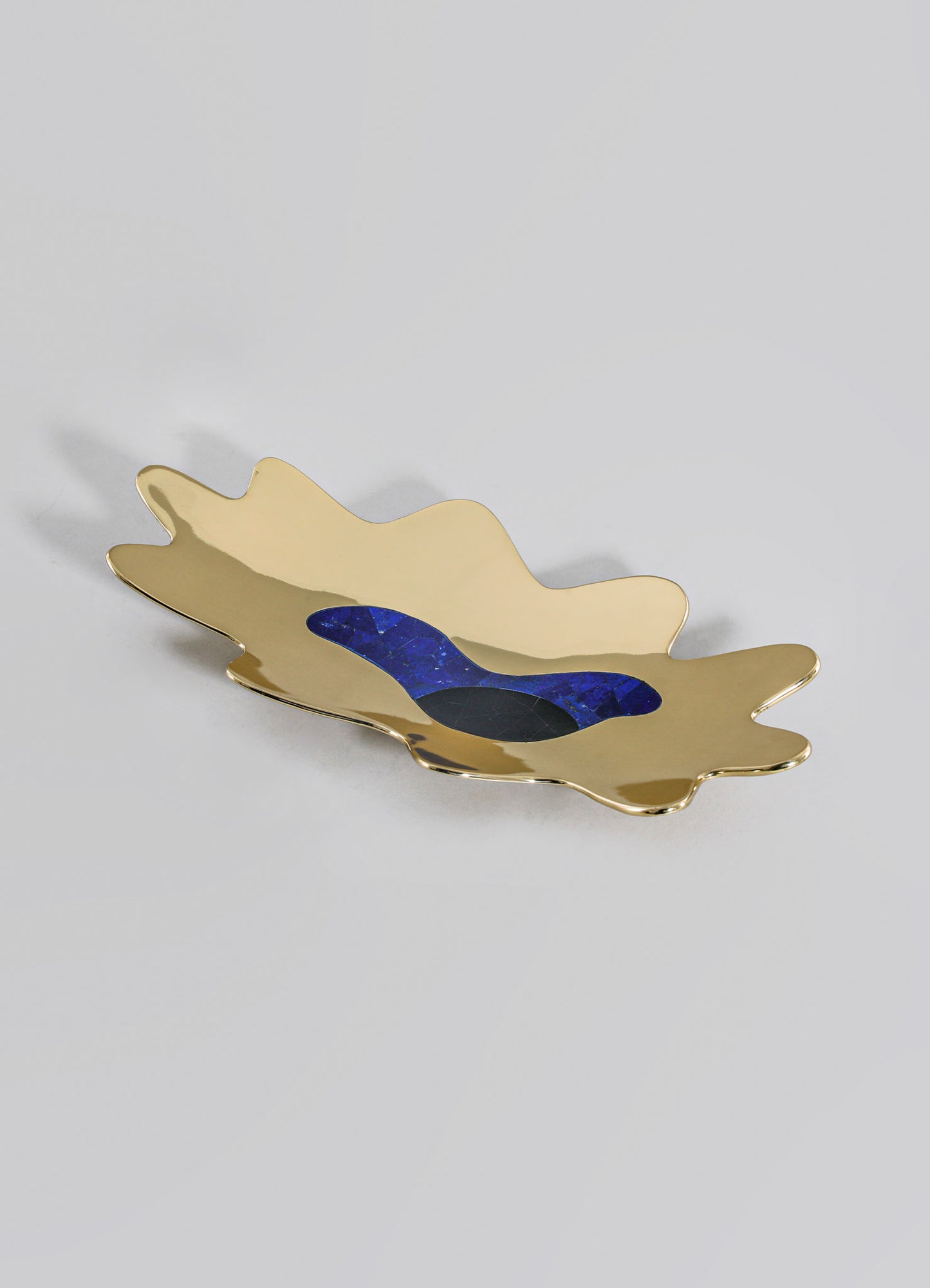 A decorative tray made of metal with a gold-tone finish, featuring an organic, irregular shape and inlaid with blue and black stone accents.