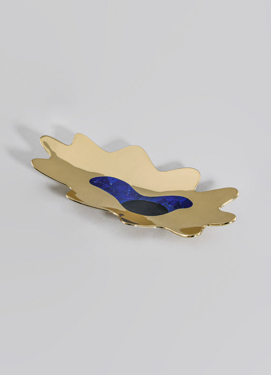 A decorative tray made of metal with a gold-tone finish, featuring an organic, irregular shape and inlaid with blue and black stone accents.