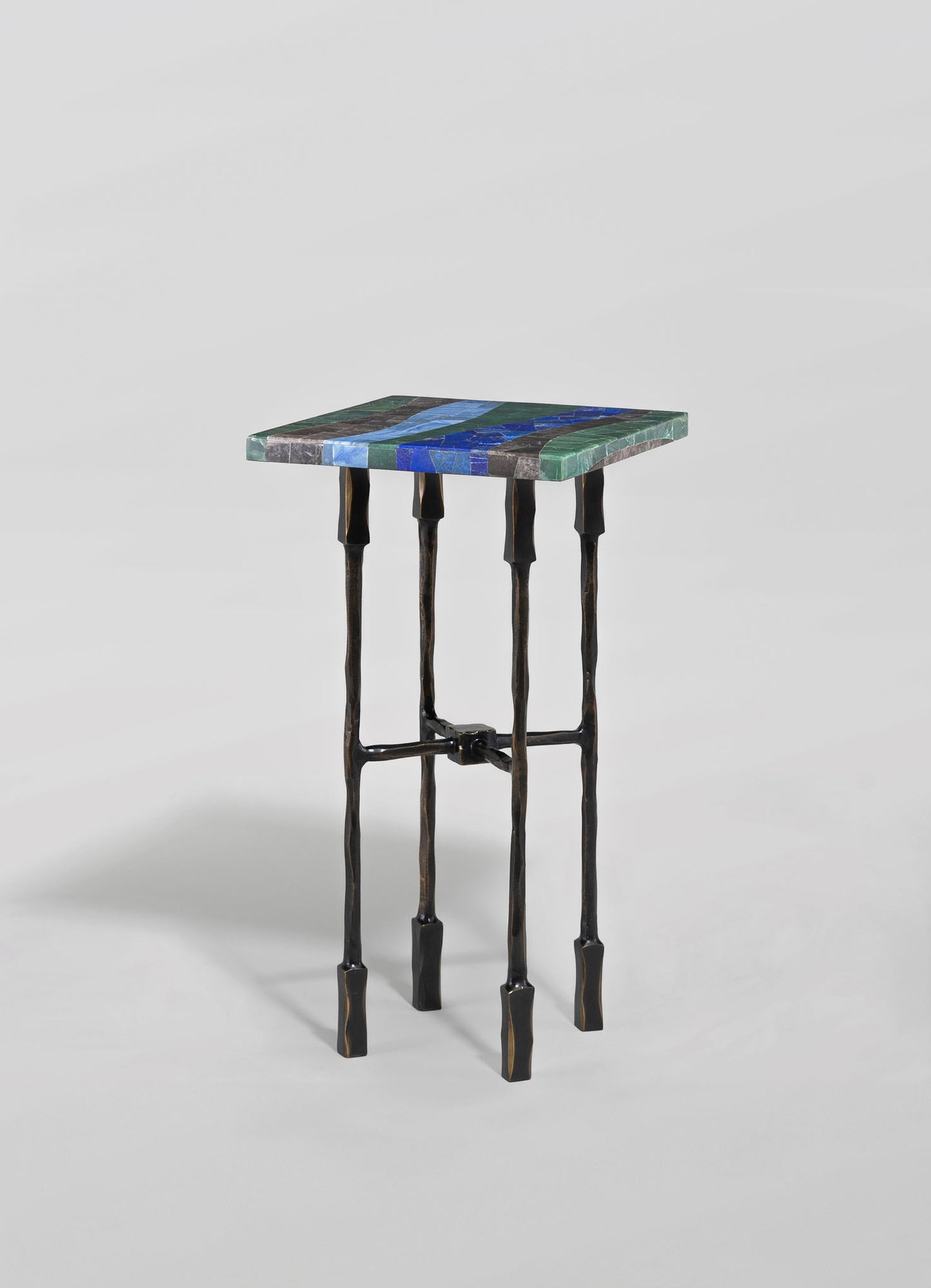 A small side table with a colorful mosaic tiled top featuring blue, green, and gray shades, and black wrought iron legs with an uneven, handcrafted appearance.