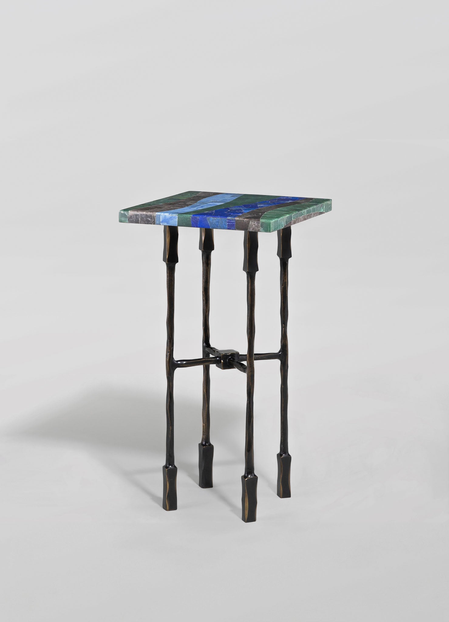 A small side table with a colorful mosaic tiled top featuring blue, green, and gray shades, and black wrought iron legs with an uneven, handcrafted appearance.