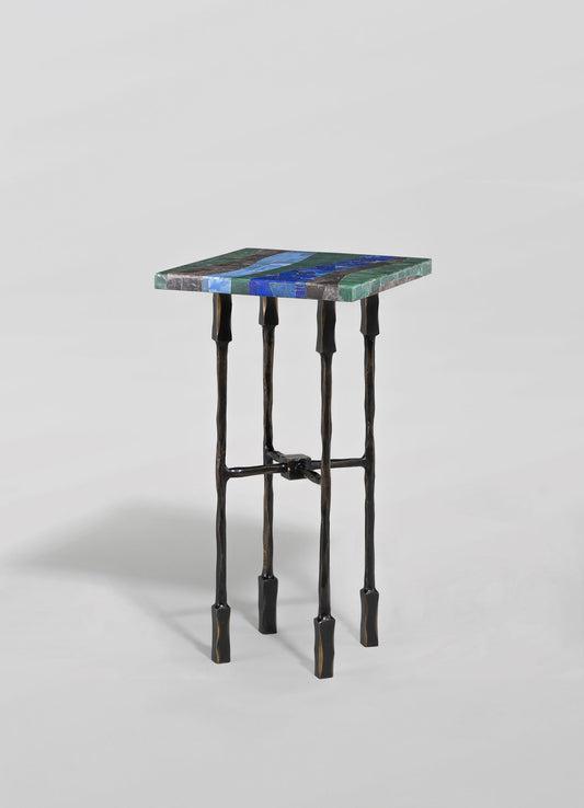 A small side table with a colorful mosaic tiled top featuring blue, green, and gray shades, and black wrought iron legs with an uneven, handcrafted appearance.
