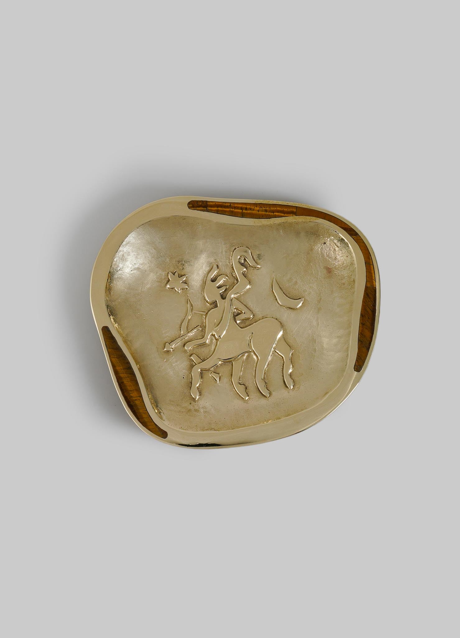 A decorative brass tray with an engraved lion motif, featuring a distressed gold finish and rounded irregular edges with wooden accents.