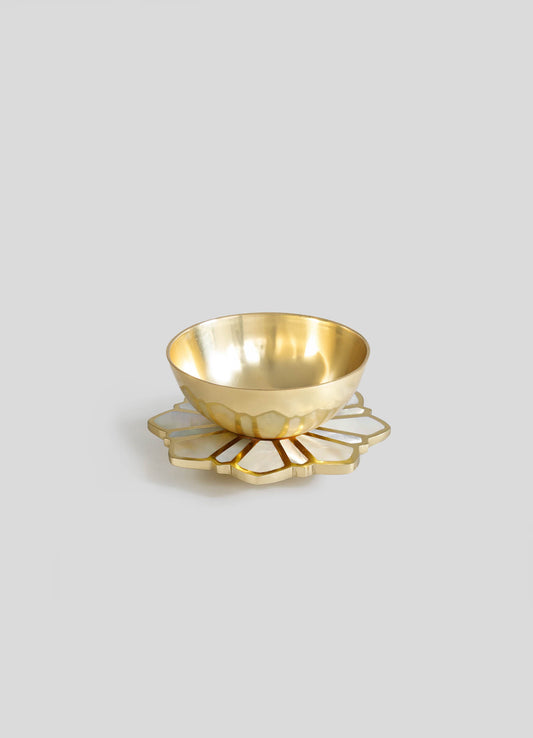 A gold-colored bowl with a smooth, reflective interior and a scalloped exterior, placed on a decorative tray with a floral motif and white inlay accents.