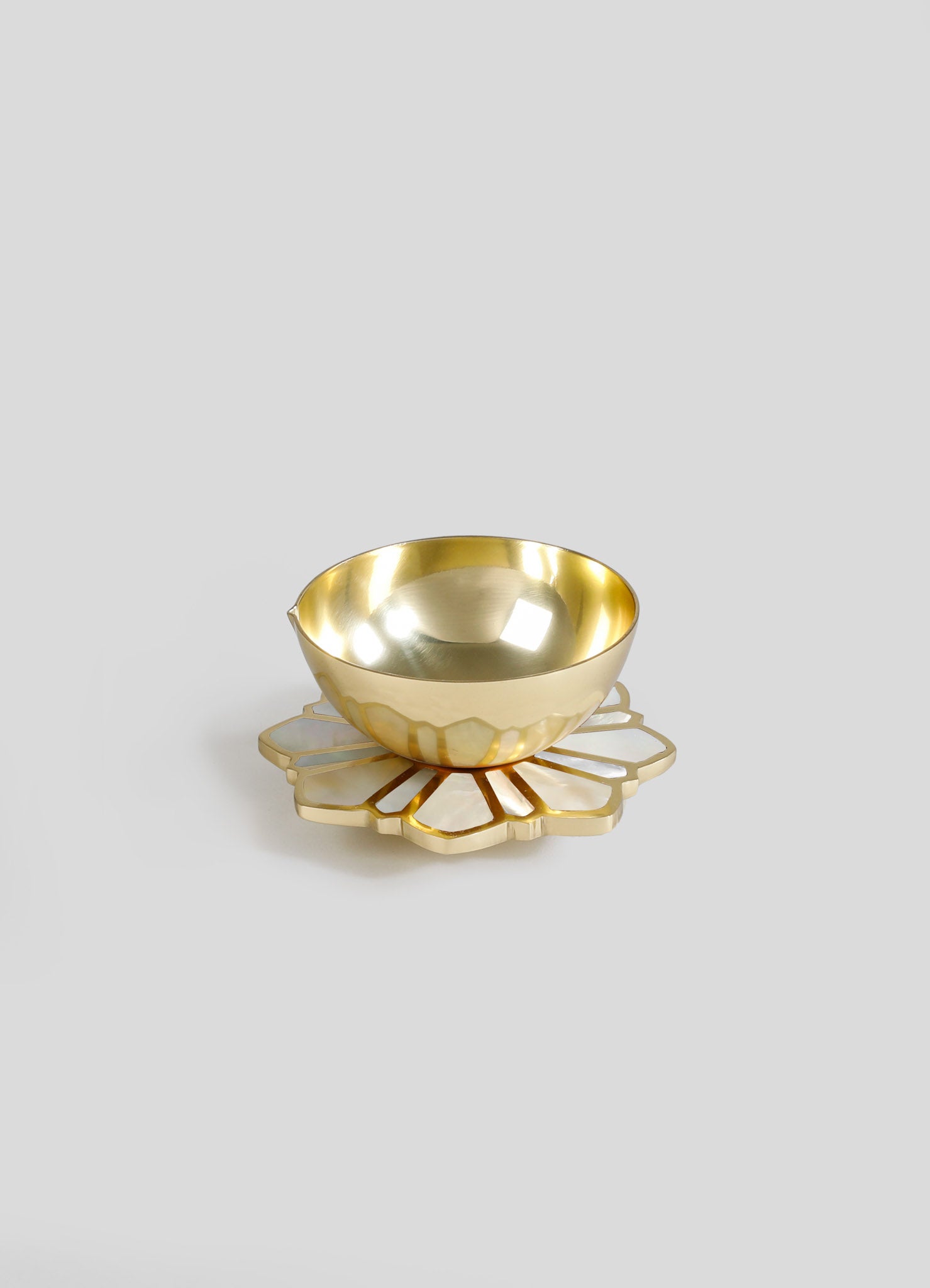 A gold-colored metal bowl with a smooth, reflective surface and a rounded shape, placed on a decorative placemat with a geometric floral pattern and a pearlescent finish.