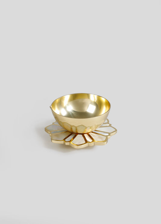 A gold-colored metal bowl with a smooth, reflective surface and a rounded shape, placed on a decorative placemat with a geometric floral pattern and a pearlescent finish.