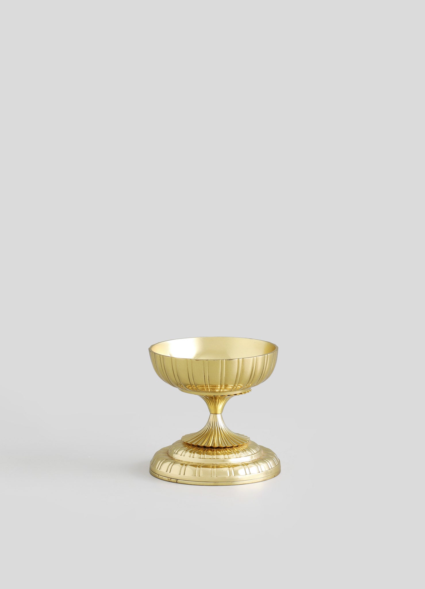 A decorative brass bowl with a fluted design, featuring a shiny gold finish and a wide, shallow shape on a short pedestal base.