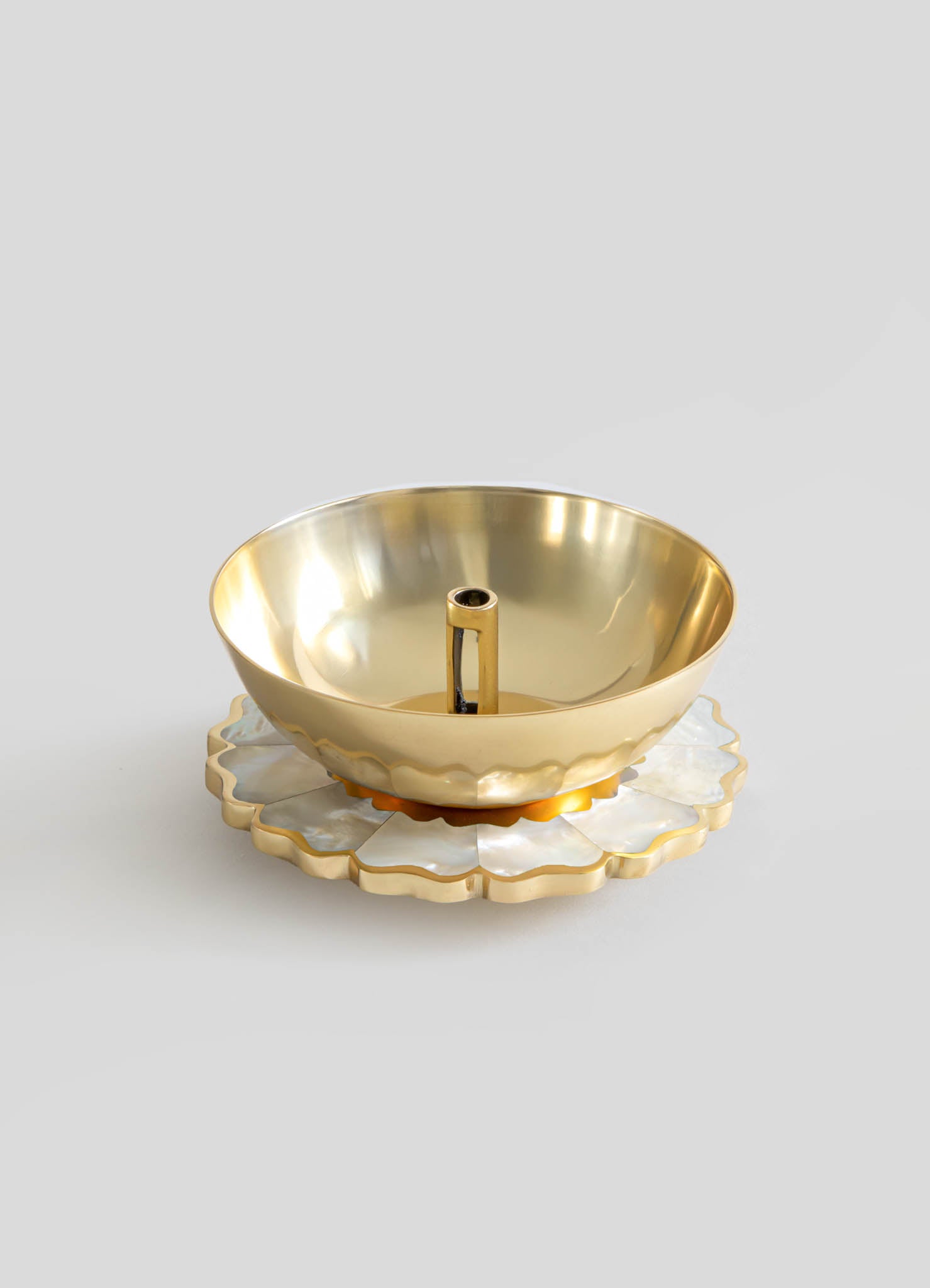 A gold-colored metal bowl with a smooth, reflective surface sits on a layered, scalloped-edge base made of iridescent material, resembling mother-of-pearl. The design is elegant and ornamental, suitable for decorative or functional use.
