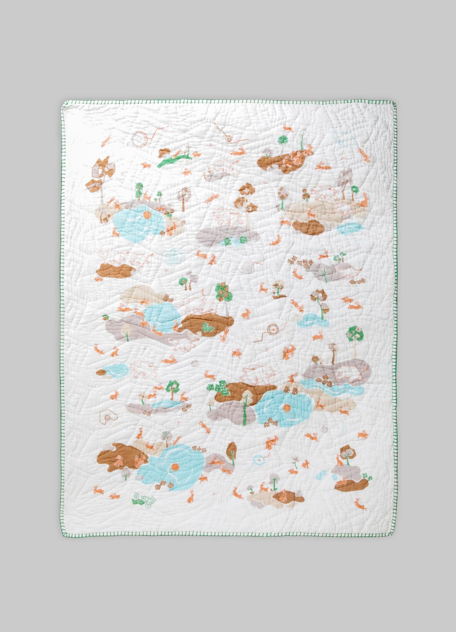 Quilt with a playful, illustrative print featuring animals, trees, and water elements in pastel shades of blue, brown, and green on a white background, bordered with a green stitched edge.
