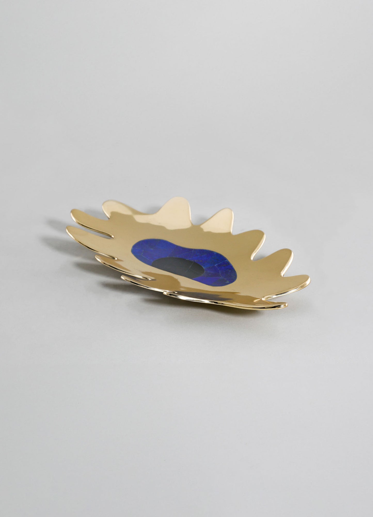 A decorative tray with an organic, leaf-like shape in metallic gold finish, featuring a blue and black marble center detail, placed on a plain light background.