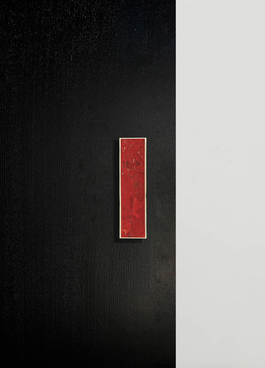 A modern wall art piece featuring a vertical rectangular marble tile with red and gold veining set against a black textured background with a narrow beige border. The artwork has a contemporary and minimalist style.