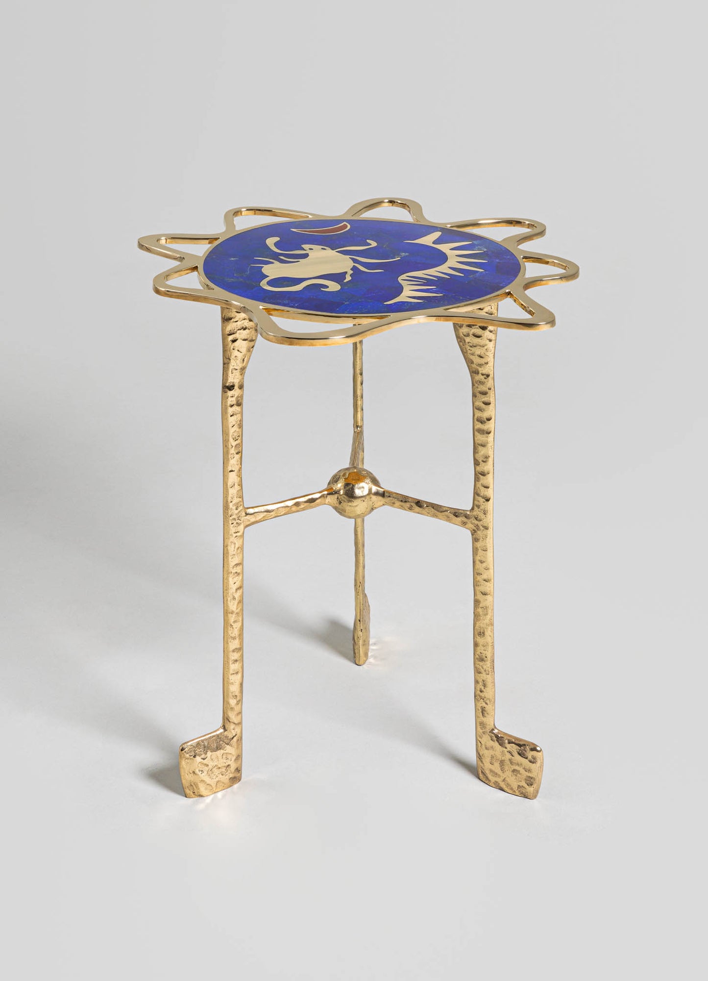 A decorative side table with a brass frame featuring textured, hammered legs and a circular blue inlay top with a gold dragon motif. The design combines contemporary and artisanal styles with metallic gold accents and intricate detailing.