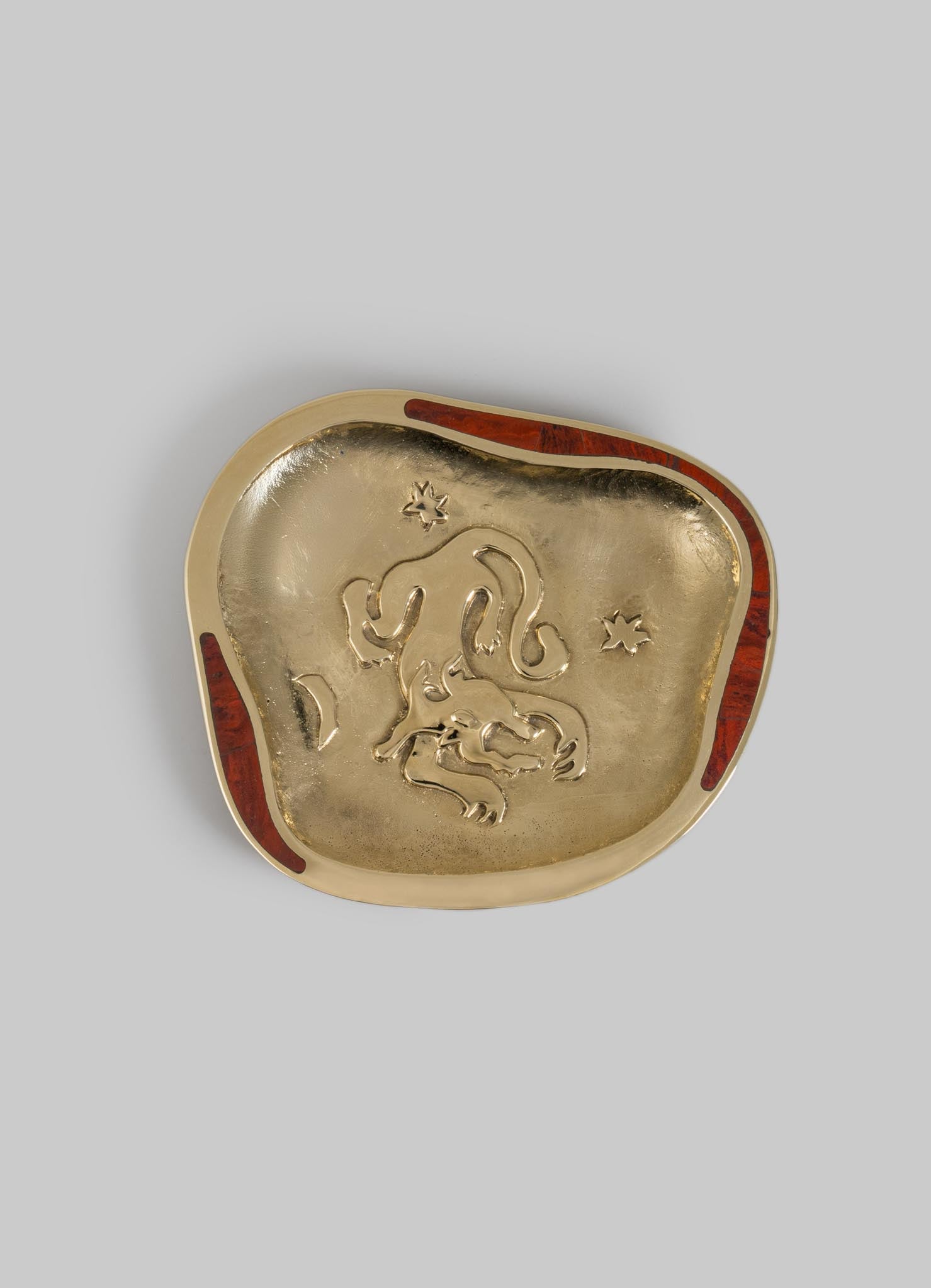A decorative metal dish with an embossed lion motif in the center, featuring a gold finish and irregular, organic shape with reddish-brown accents along the rim.