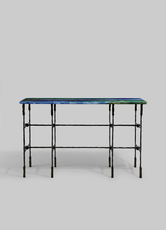 A console table with a colorful tiled top featuring geometric patterns in shades of blue, green, and teal. The table has a black wrought iron frame with a rustic, handcrafted appearance and a minimalist, contemporary style.