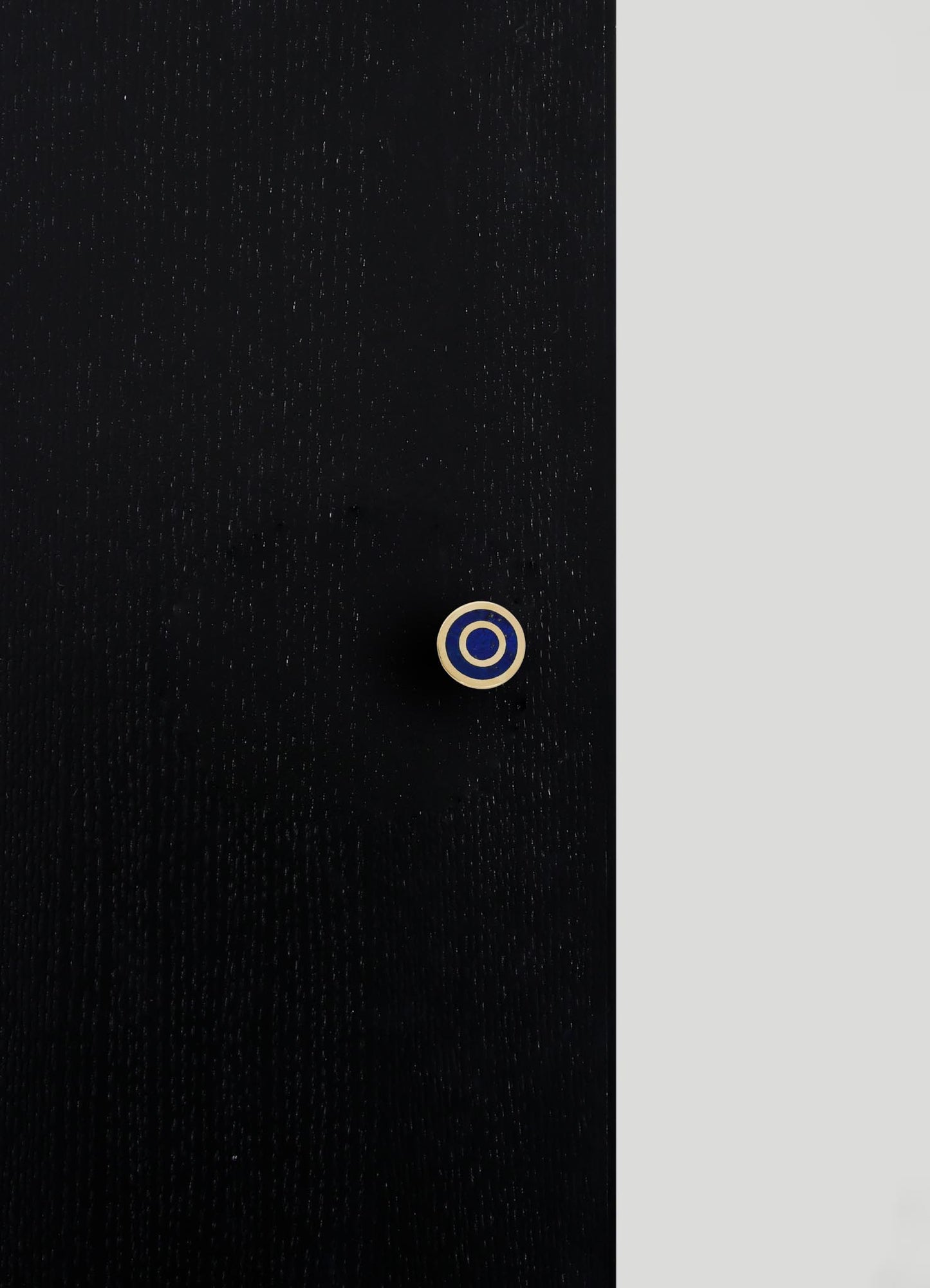 A close-up of a black fabric with a subtle textured pattern, featuring a small circular button with concentric rings in beige and navy blue.
