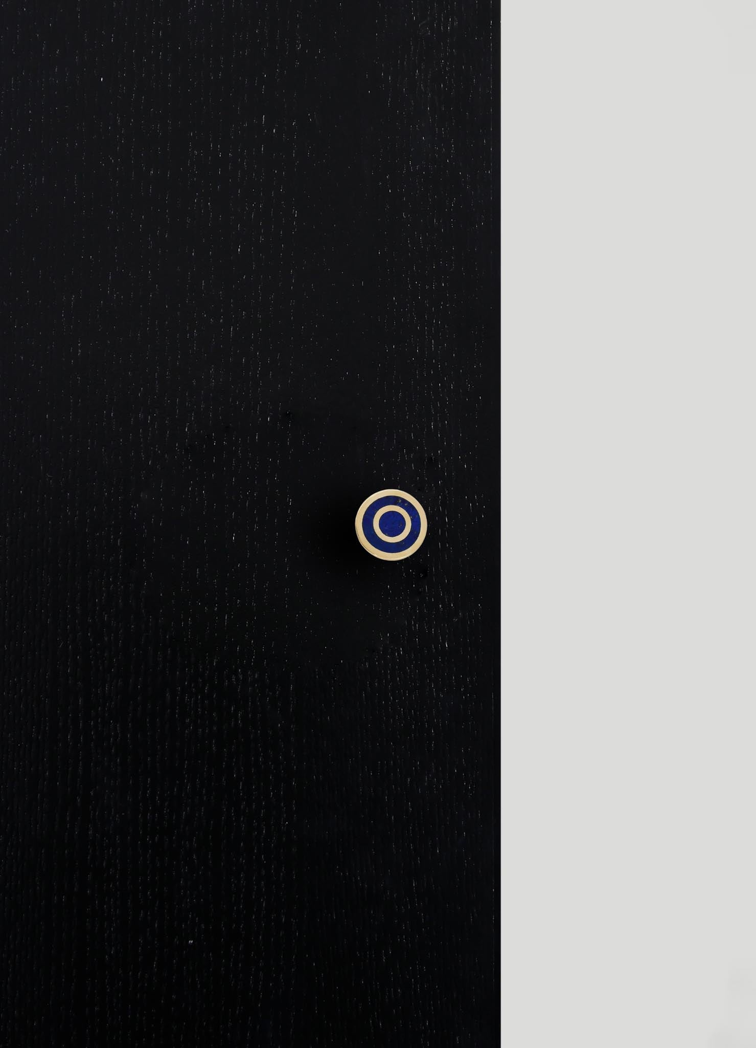 A close-up of a black fabric with a subtle textured pattern, featuring a small circular button with concentric rings in beige and navy blue.