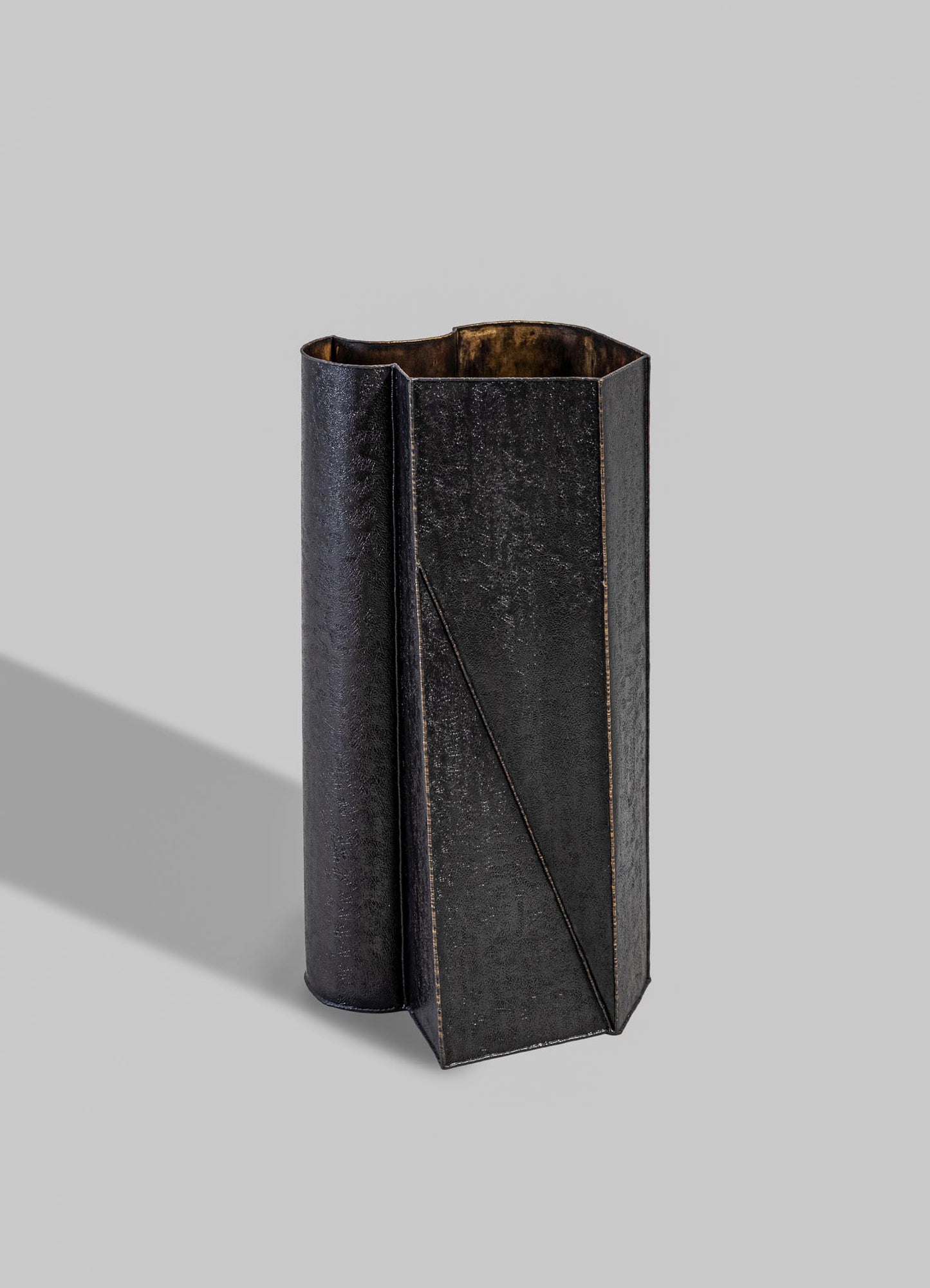 A tall, black metal vase with a textured, matte finish and angular geometric design, featuring a subtle diagonal line detail.