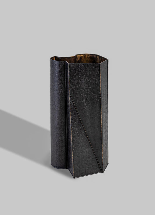 A tall, black metal vase with a textured, matte finish and angular geometric design, featuring a subtle diagonal line detail.