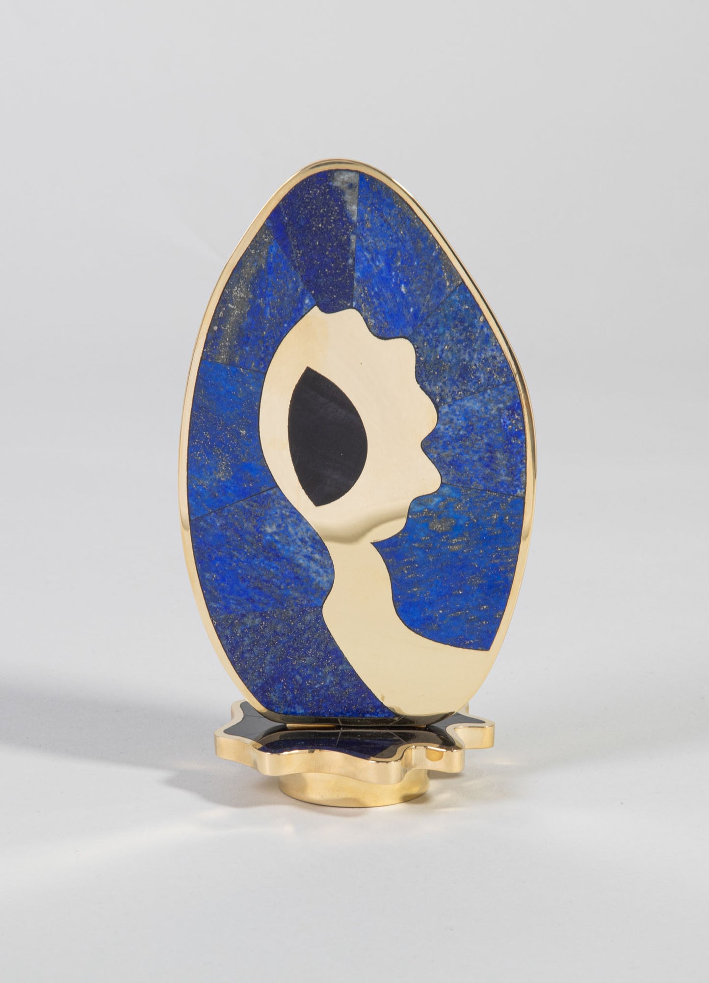 Decorative sculpture featuring an abstract face profile with a combination of beige and black tones, set on a gold-colored metal base. The piece has a modern-art style with smooth curves and contrasting colors.