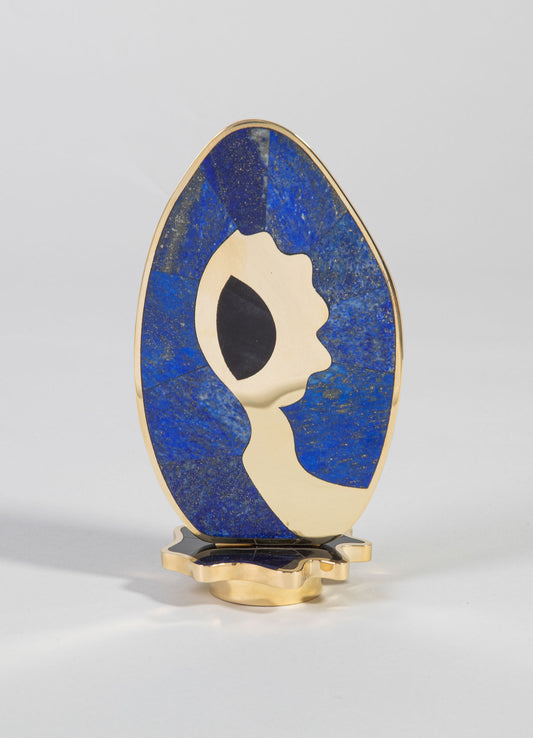 Decorative sculpture featuring an abstract face profile with a combination of beige and black tones, set on a gold-colored metal base. The piece has a modern-art style with smooth curves and contrasting colors.