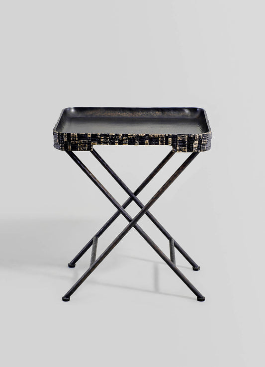 A black metal tray with a textured, carved pattern edge, mounted on a minimalist X-shaped metal stand.