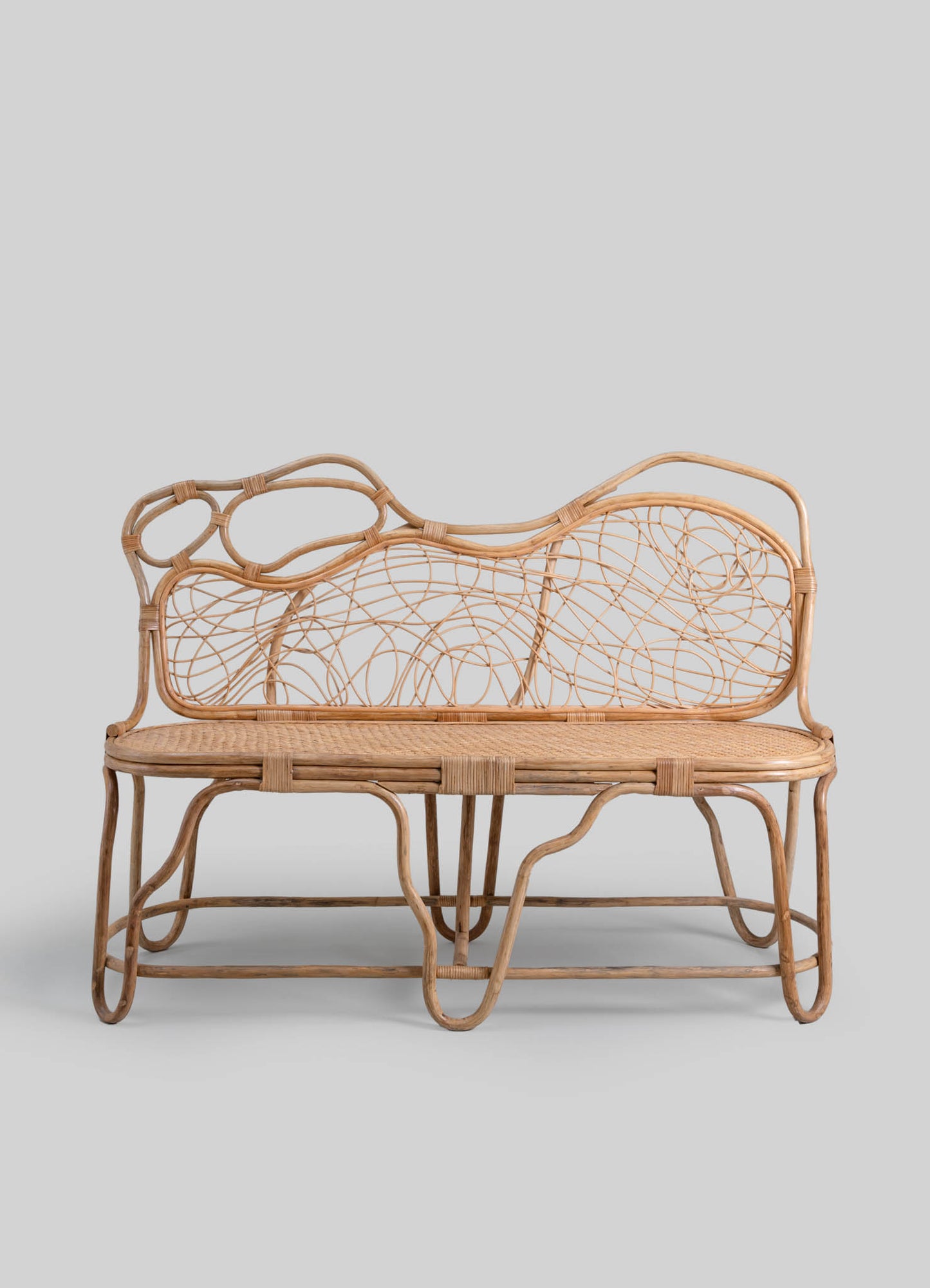 Wicker bench with a natural wood finish featuring an abstract, organic pattern on the backrest and a woven seat, set against a plain background.