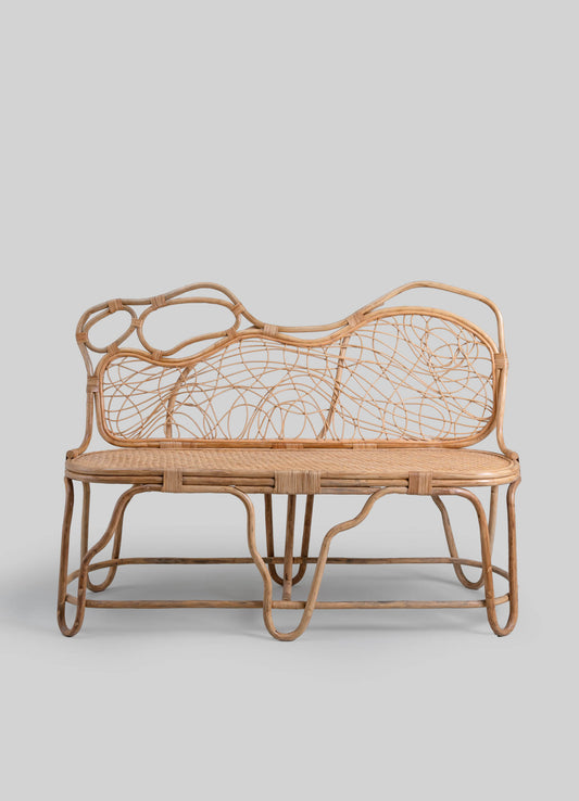 Wicker bench with a natural wood finish featuring an abstract, organic pattern on the backrest and a woven seat, set against a plain background.