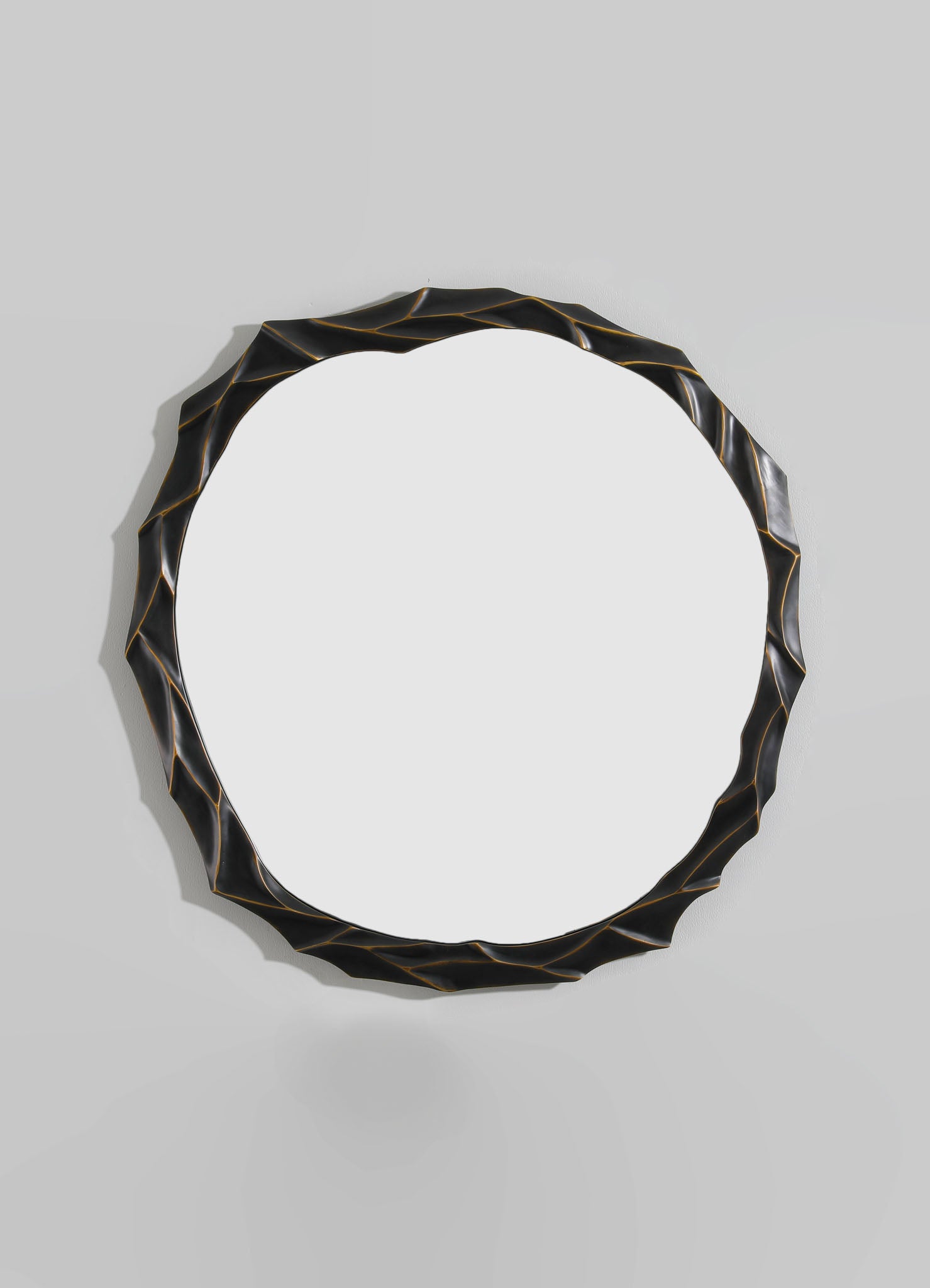 A decorative round mirror with a black and gold-finished irregular, textured frame, mounted on a plain light-colored wall.