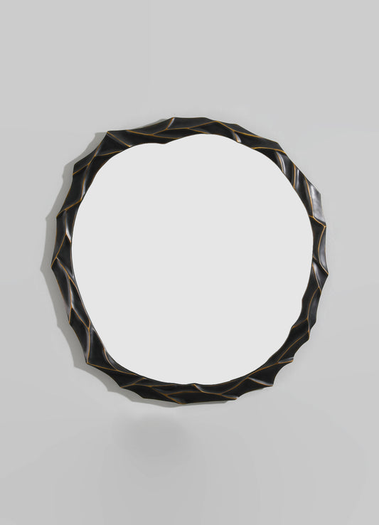 A decorative round mirror with a black and gold-finished irregular, textured frame, mounted on a plain light-colored wall.