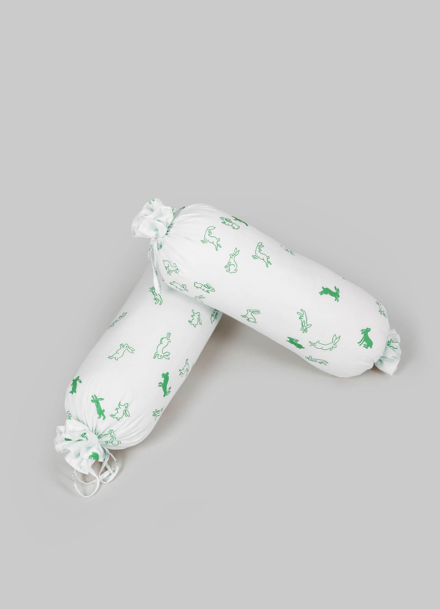Two fabric bolster pillows with white base and green bunny and rabbit motifs, featuring ruching and tie closures at each end.