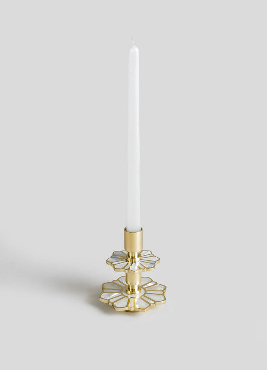 A decorative candle holder with brass and mother-of-pearl inlay, featuring a floral motif and two tiered petal shapes, holding a tall white tapered candle.