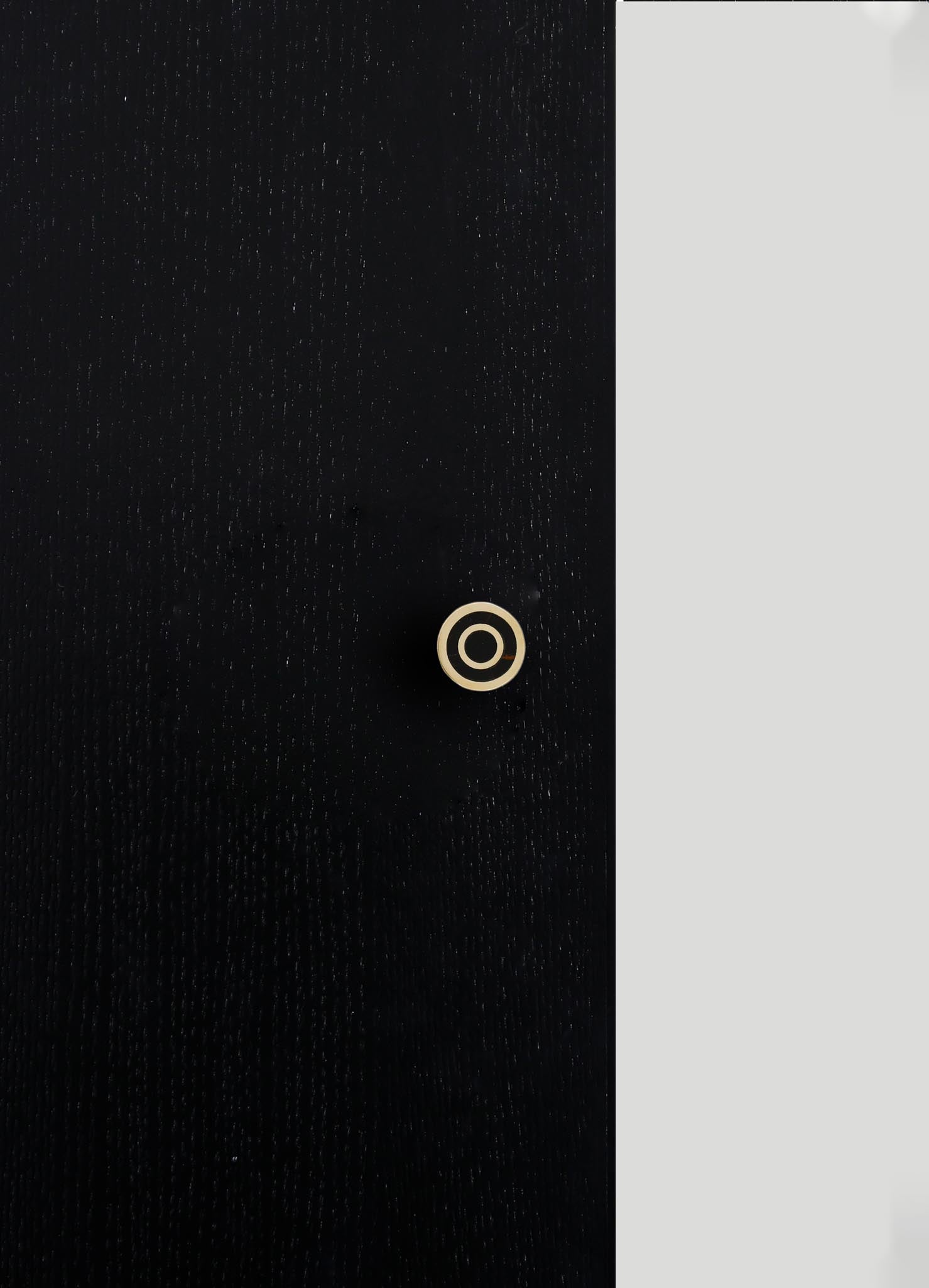 A black fabric with a subtle textured pattern and a small, concentric circular detail in beige. The fabric appears to have a smooth finish with fine stitching or weave.