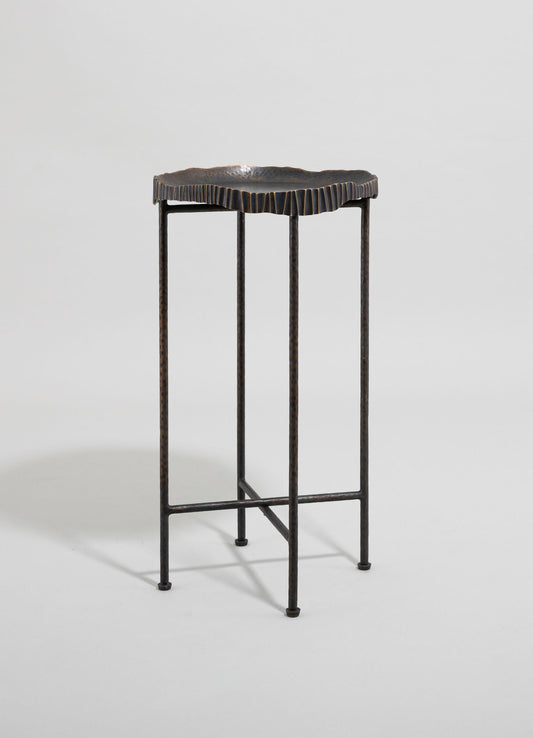 A decorative metal stand with a hammered finish and scalloped edge on the top, featuring a dark, oxidized finish and slender, textured legs.