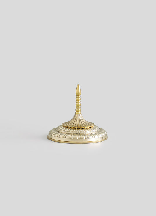 A decorative brass finial with a tiered, ribbed design and a pointed tip, mounted on a round, scalloped base with a polished finish.