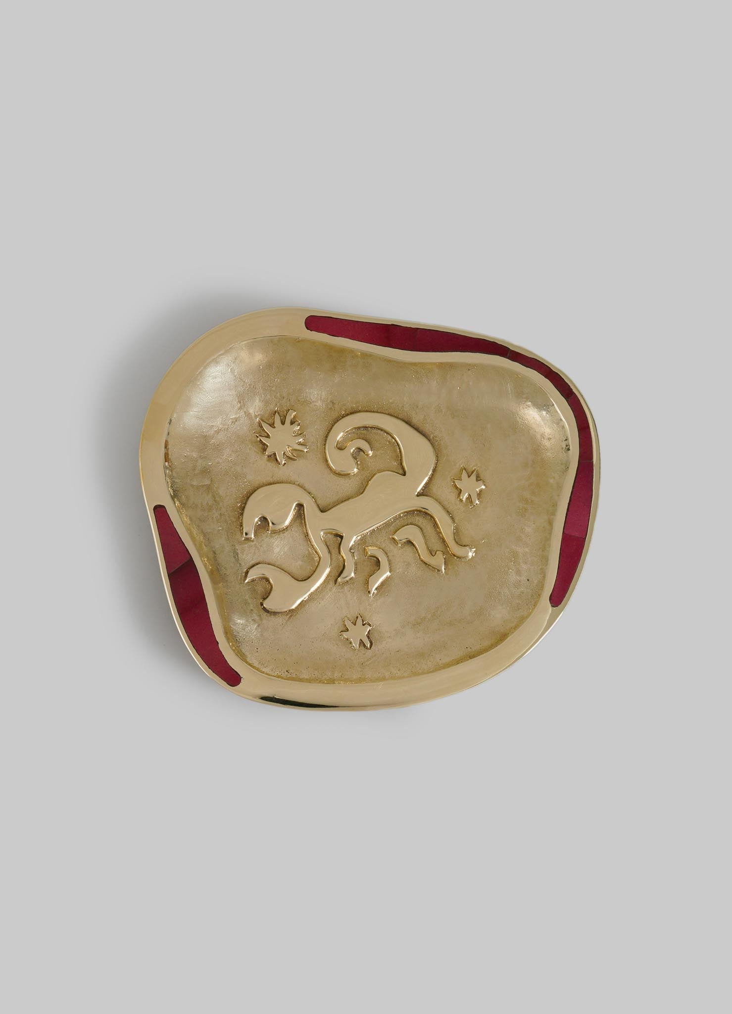 A square-shaped decorative dish featuring a metallic gold finish, with a carved animal motif and star and sun symbols, accented by a red border. The dish has a textured surface and appears handcrafted with a rustic, artisanal style.