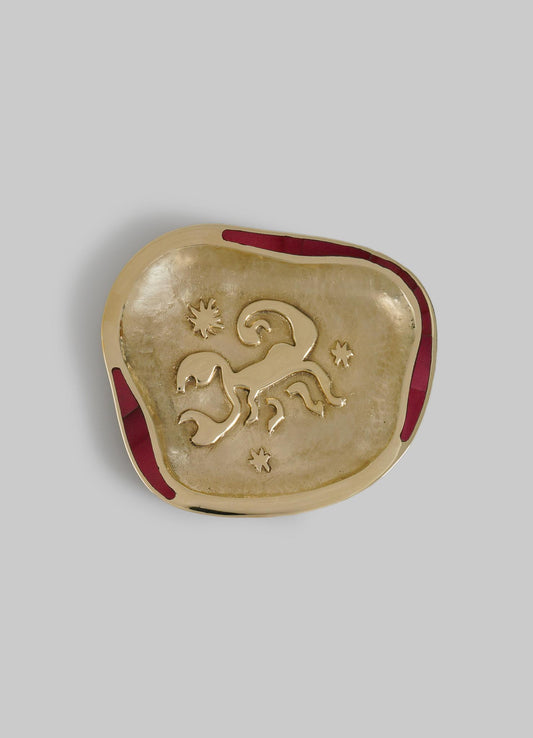 A square-shaped decorative dish featuring a metallic gold finish, with a carved animal motif and star and sun symbols, accented by a red border. The dish has a textured surface and appears handcrafted with a rustic, artisanal style.