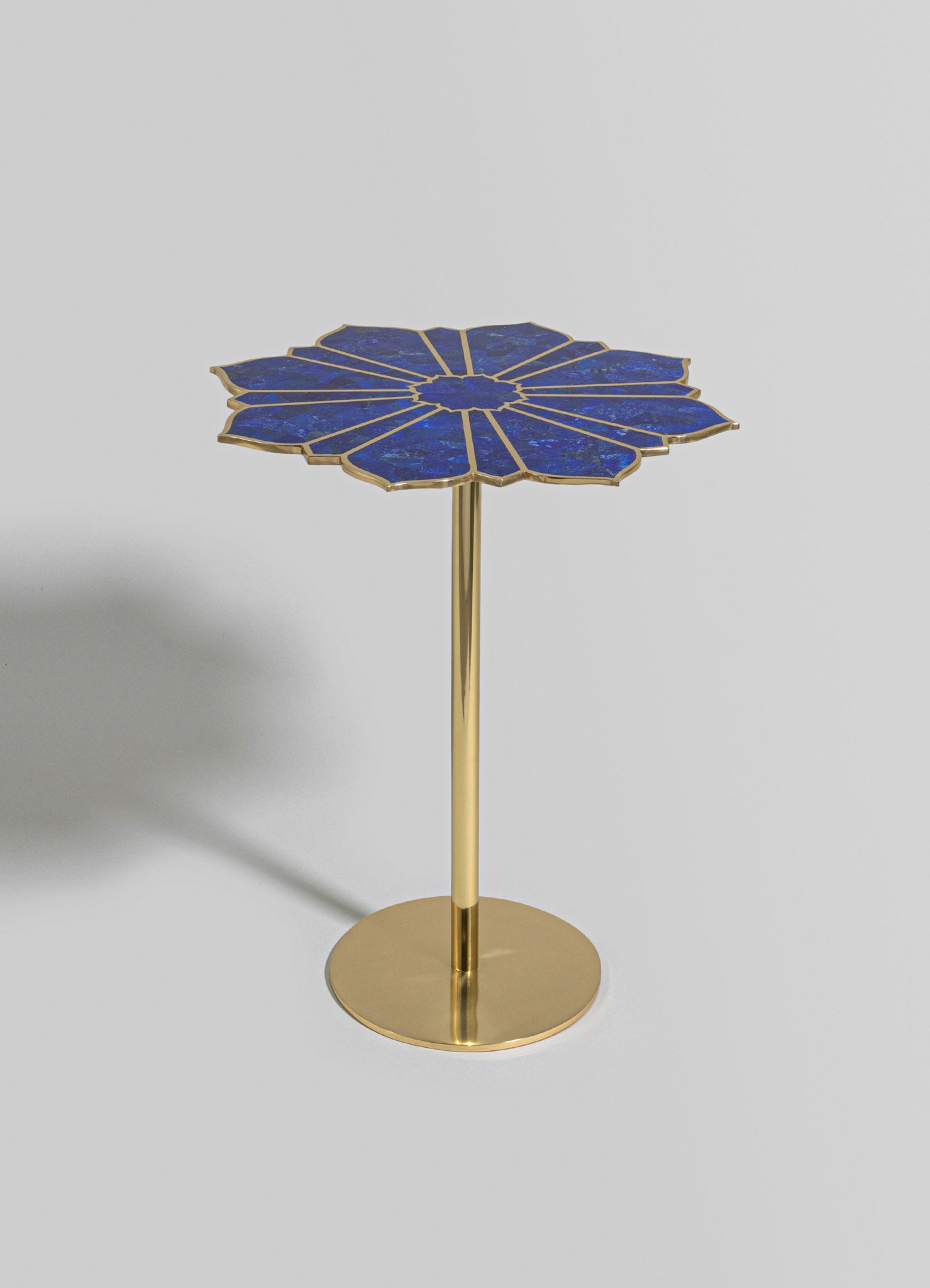 A side table with a blue lapis lazuli top featuring a flower-like radiating pattern, edged with a metallic gold finish. The table has a slender gold metal stem and a round gold base, combining luxurious materials with a contemporary style.