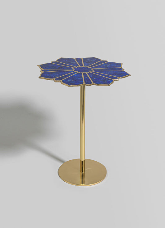 A side table with a blue lapis lazuli top featuring a flower-like radiating pattern, edged with a metallic gold finish. The table has a slender gold metal stem and a round gold base, combining luxurious materials with a contemporary style.