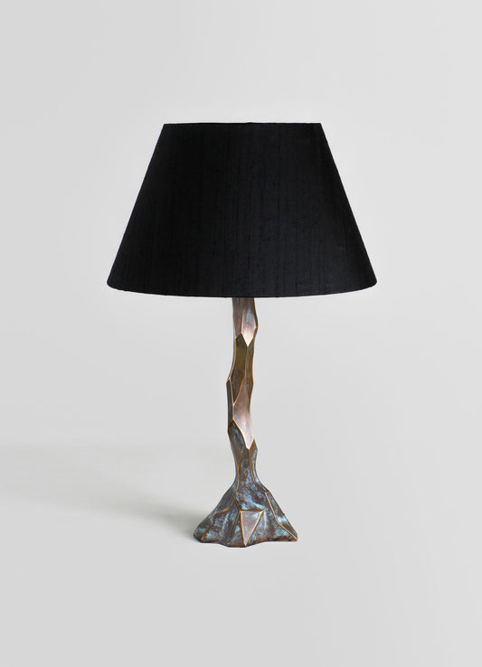 A table lamp with a sculptural base featuring an irregular, geometric metallic finish and a black fabric lampshade.