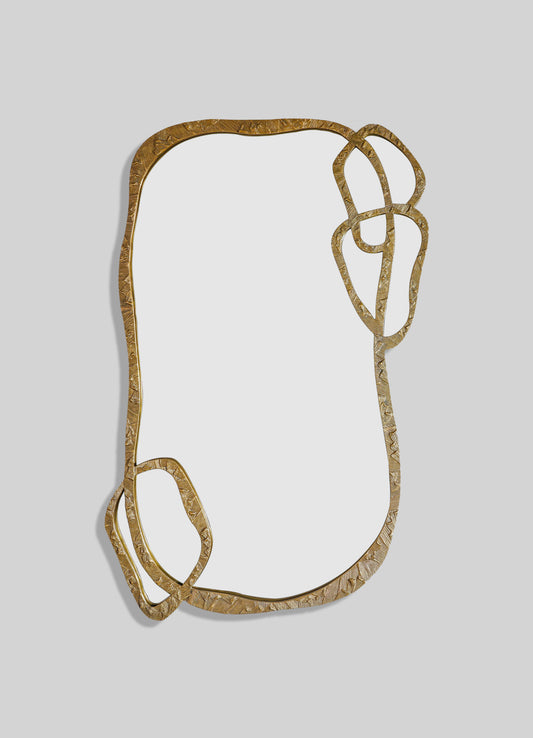 A decorative mirror frame made of textured brass with an irregular, organic shape and abstract, curving motifs. The frame has a gold-tone finish and an artistic, contemporary style.
