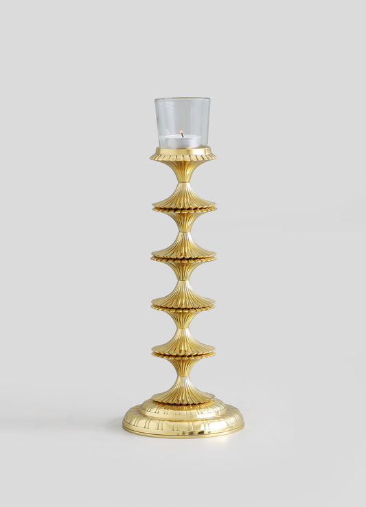 A gold-toned decorative candle holder with a fluted, shell-like motif, supporting a glass container with a white candle inside. The design features ornate, layered details with a shiny metallic finish, creating a luxurious and elegant aesthetic.