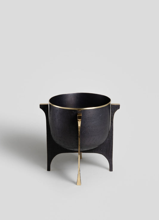 A black bowl with a textured surface, accented by gold trim and a vertical gold detail, rests on a black wooden stand with curved legs. The design combines modern and luxurious elements with a focus on metallic contrasts.