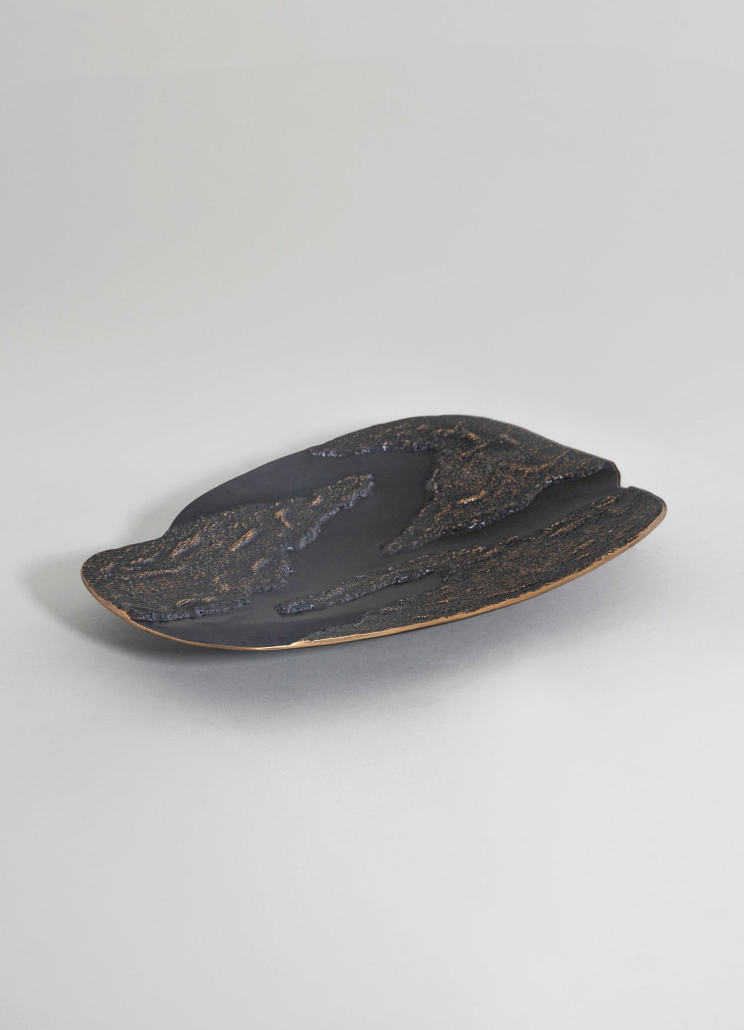 A decorative ceramic tray with a black matte surface and textured gold accents, featuring an organic, flowing shape on a neutral background.
