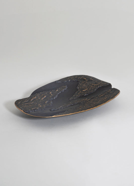 A decorative ceramic tray with a black matte surface and textured gold accents, featuring an organic, flowing shape on a neutral background.
