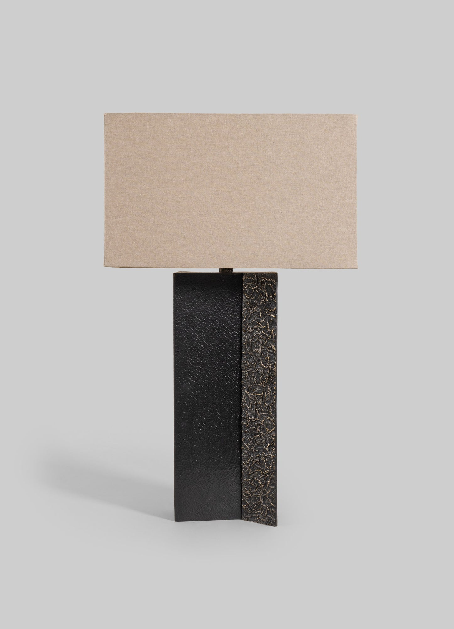 A table lamp with a rectangular beige fabric shade and a black textured base featuring a gold-toned, cracked surface finish.