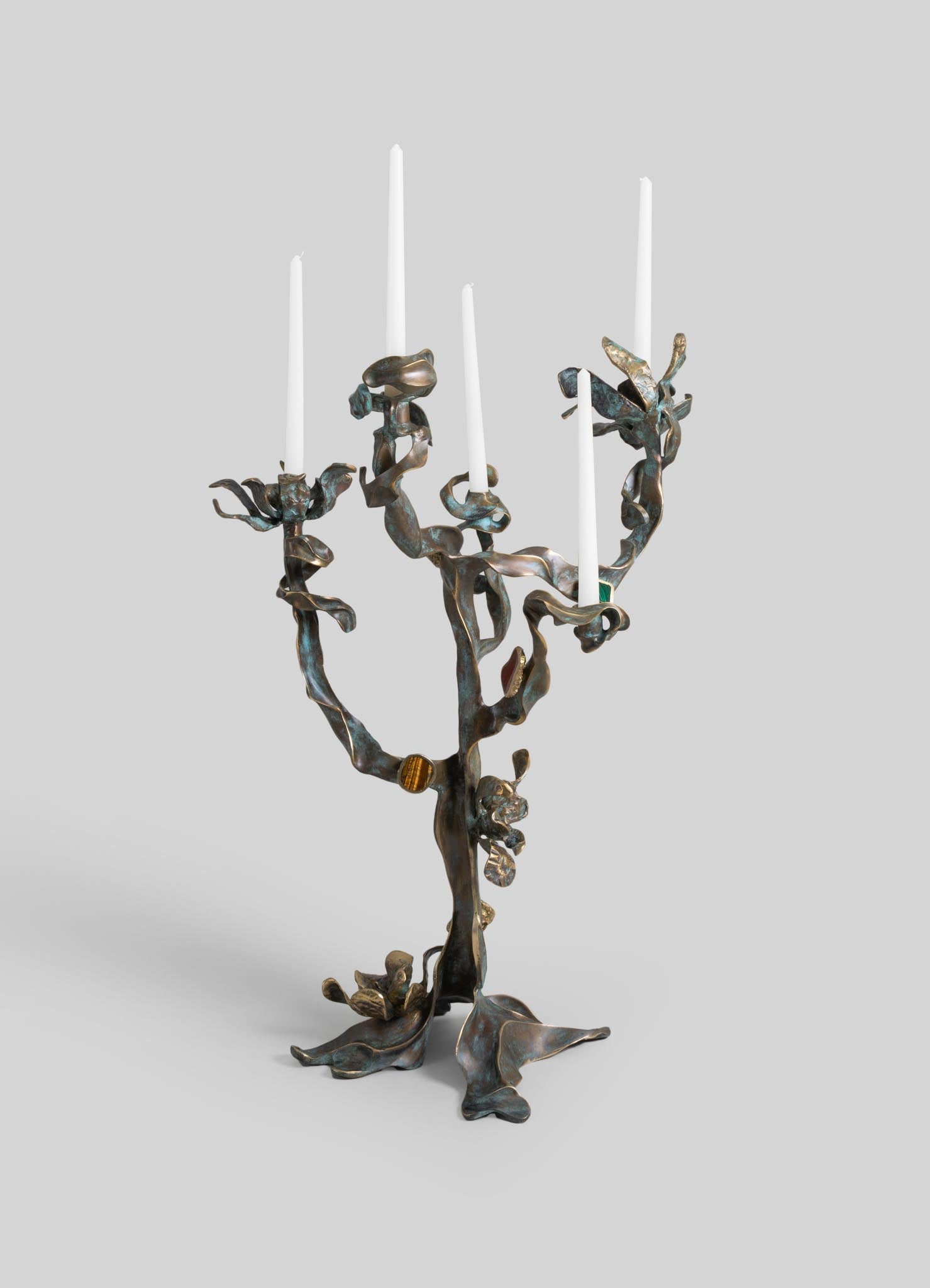 Metallic bronze candelabra with a sculptural, organic design resembling flowing branches or vines, holding five white taper candles. The piece has a handcrafted, artistic style with a natural, rustic aesthetic.