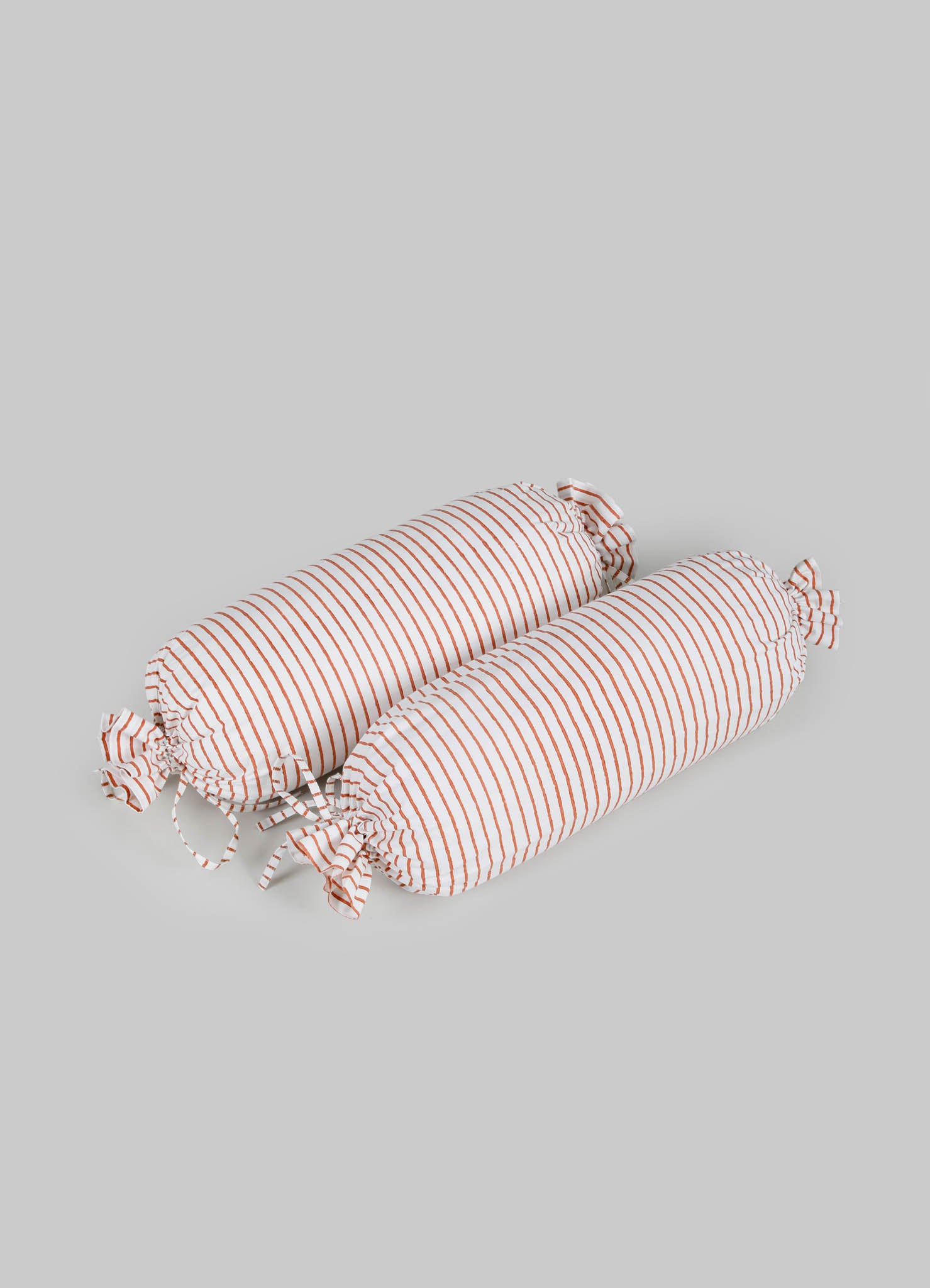 Striped fabric bolster cushions with orange and white narrow lines, featuring gathered fabric ties at each end, made of soft textile material.