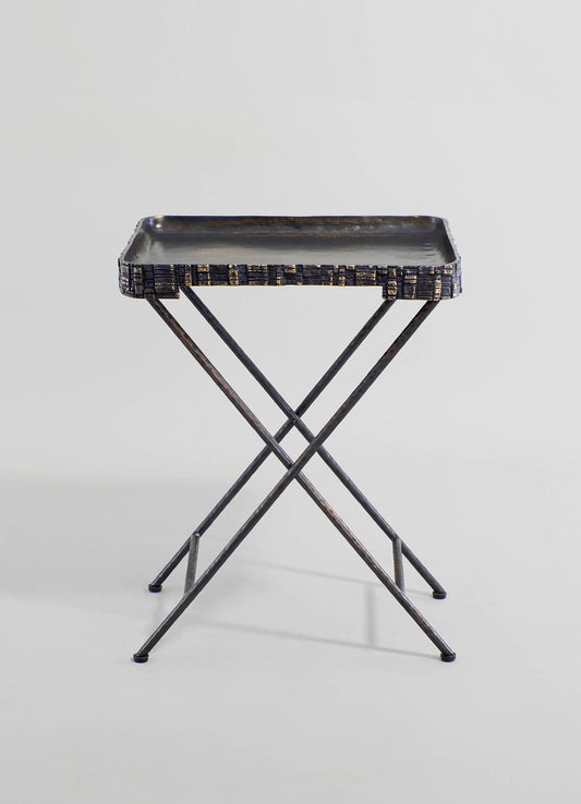 A metal tray with a textured, geometric pattern along the edges, supported by a cross-legged metal stand with a dark finish. The overall design has an industrial and minimalist style.