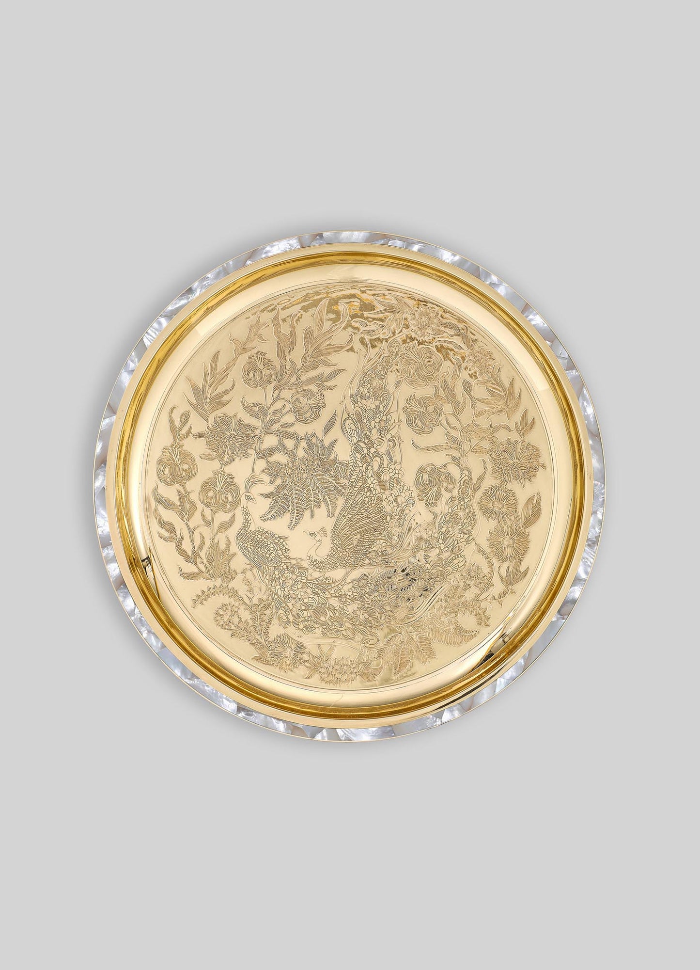 A round decorative tray made of gold-toned metal with intricate engraved floral and peacock motifs, bordered by a clear, faceted acrylic edge.